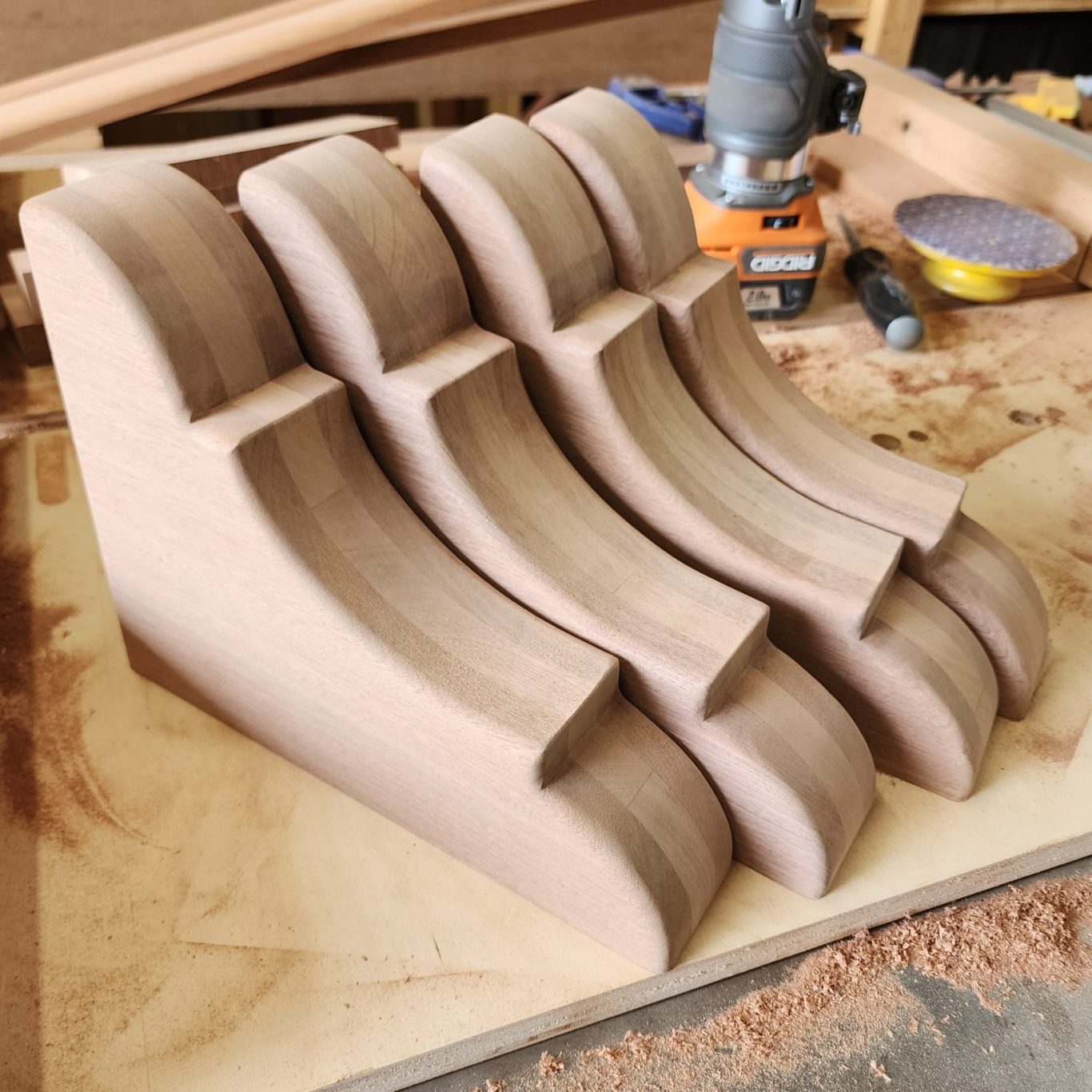 Wood Corbels Several wooden corbels arranged side by side on a workbench beneath a router.