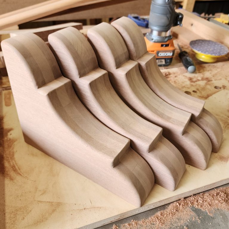 Millwork Custom wood corbels with shaped profiles arranged on a workbench.