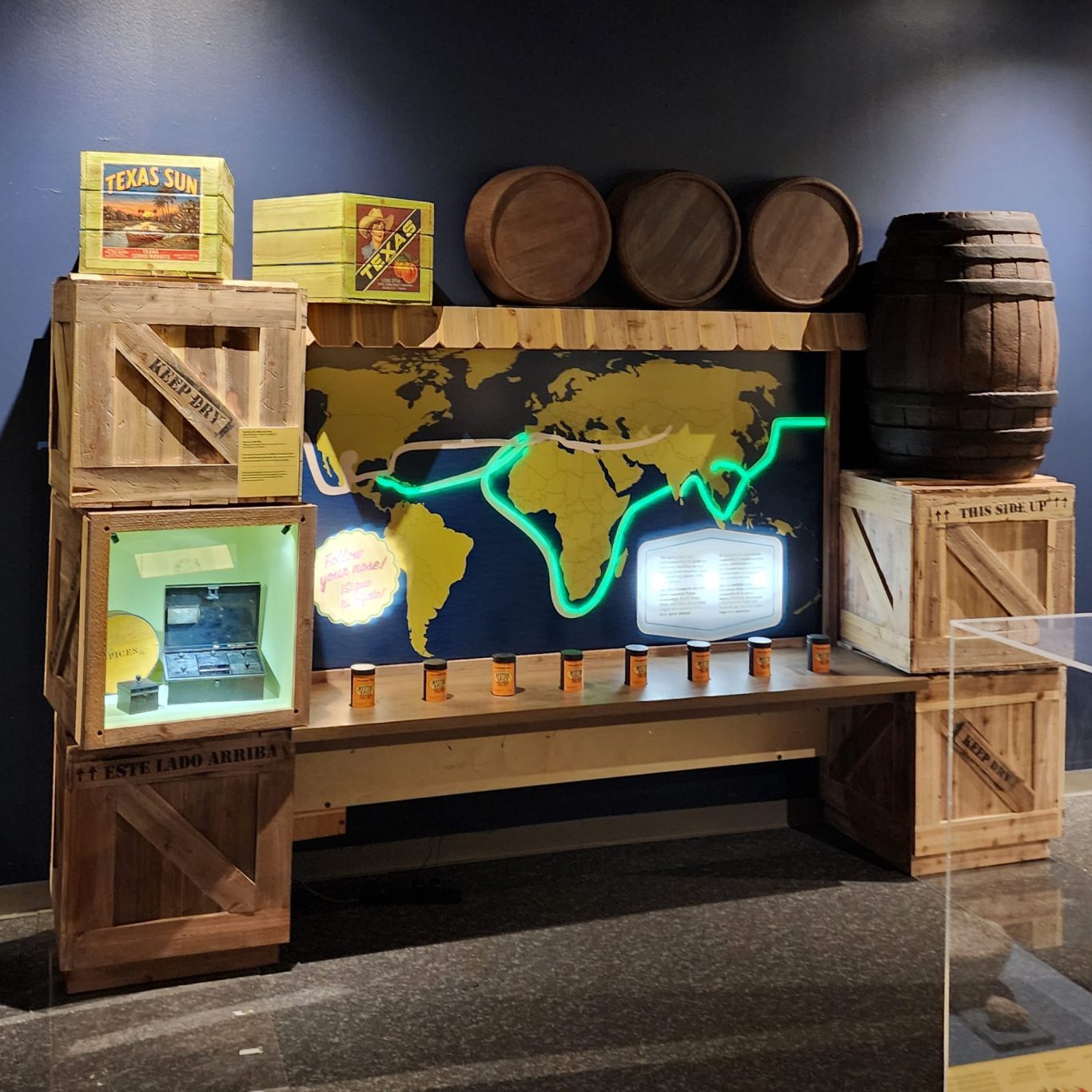 Spice Routes Exhibit Museum display with a glowing world map, wooden crates, barrels, shelves, and spice cans.