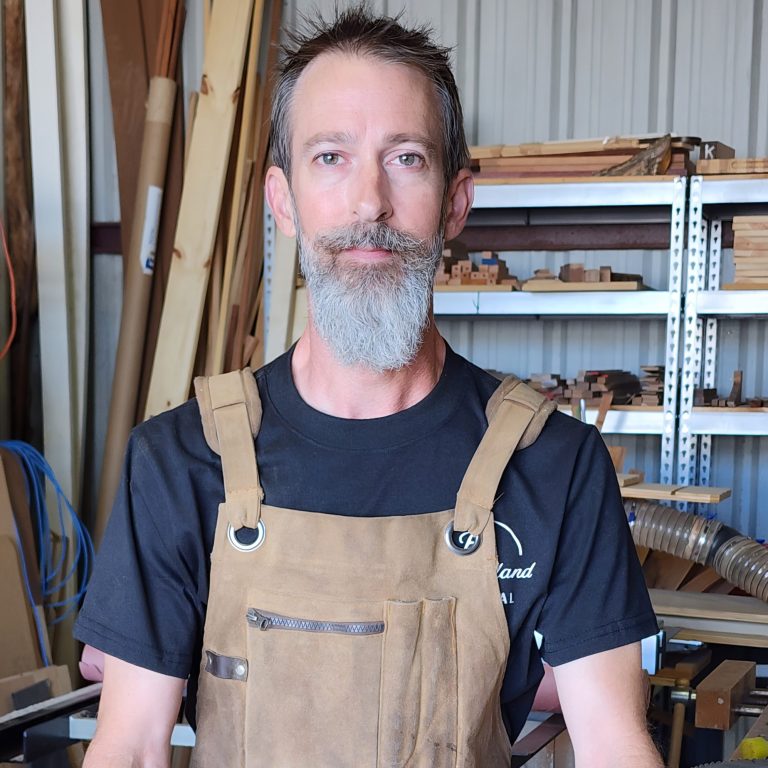 Kevin Pruitt in the Studio Kevin Pruitt wearing a work apron and standing in his woodworking studio.